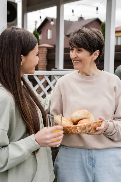 Modern parenting, celebration of parents day, happy middle aged mother holding buns and talking with her teenage daughter, modern parenting, suburban life, summer, family house — Stock Photo