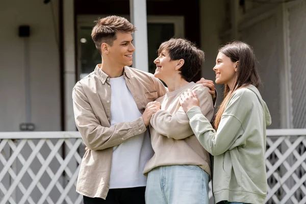 Happy parents day, cheerful son and teenage daughter hugging cheerful middle aged mother on backyard of family house, celebration, bonding, candid, modern parenting, moments to remember — Stock Photo