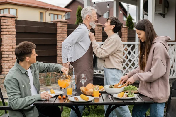 Happy middle aged couple looking at each other during family bbq party, young adult son looking at cheerful parents, love, joyful teenage girl mixing salad, happy parents day, backyard, summer — Stock Photo