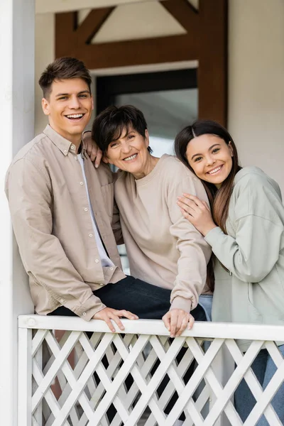 Parents day concept, middle aged woman smiling with cheerful daughter and son on porch of summer house, looking at camera, family reunion, bonding, modern parenting, moments to remember — Stock Photo
