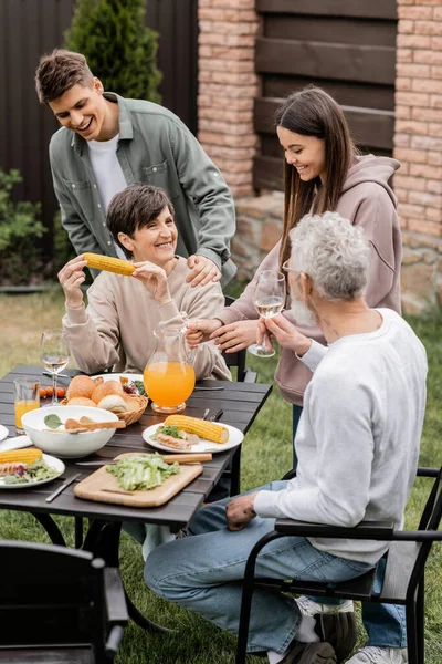 Smiling siblings standing near middle aged mother and father during family barbeque in relaxed atmosphere during parents day celebration at backyard, family love and unity concept — Stock Photo