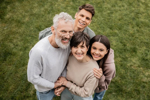 Overhead view of cheerful children hugging middle aged parents and looking at camera while celebrating parents day together at backyard in june, quality time with parents concept — Stock Photo