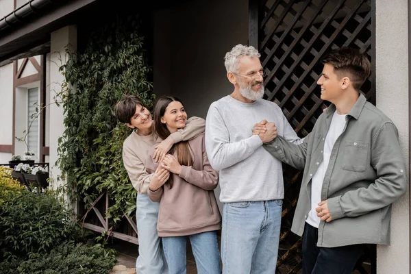 Positivo padre di mezza età che stringe la mano al giovane figlio vicino alla famiglia durante la celebrazione del giorno dei genitori vicino al portico di casa in cortile, concetto di relazione genitore-figlio, occasione speciale — Foto stock