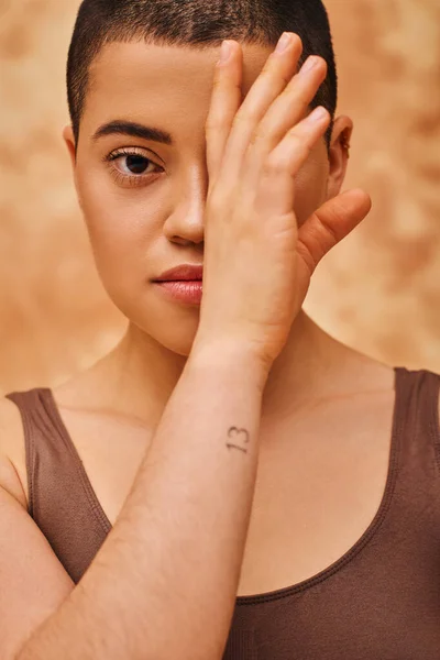 Natural look, tattooed young woman with short hair posing on mottled beige background, hand near face, individuality, modern generation z, beauty and confidence, body positivity — Stock Photo