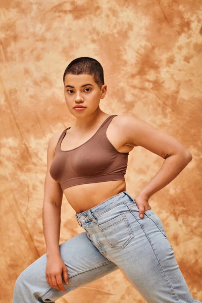 Jeans-Look, Generation Z, junge kurvige Frau mit Tätowierungen posiert mit der Hand in der Tasche auf fleckigem beigem Hintergrund, verschiedene Formen, Body Positivity Bewegung, Selbstwertgefühl, Selbstvertrauen — Stockfoto