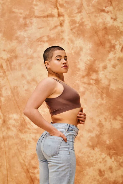 Denim fashion, gen z, young curvy woman posing on mottled beige background, different shapes, body positivity movement, self-esteem, confidence, short haired model, hand in pocket — Stock Photo