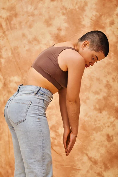 Позитивность тела, джинсовая мода, кривая и татуированная женщина в джинсах и топе на пятнистом бежевом фоне, повседневная одежда джинсовой моды, принятие себя, поколение z, разнообразие тела — стоковое фото