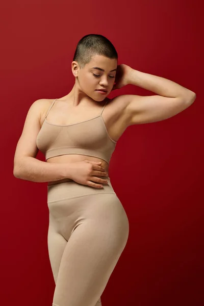 Self acceptance, young woman in beige underwear posing on red background, body positivity, curvy fashion, comfortable in skin, curvy model, generation z, self love, short hair — Stock Photo