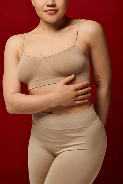 Body positive, self-esteem, cropped view of tattooed young woman posing on burgundy background, dark red, curvy fashion, comfortable in skin, female underwear, fashion model, body type — Stock Photo