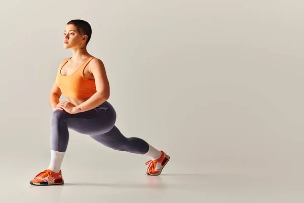 Body positivity movement, young short haired woman doing lunges on grey background, curvy fitness model in sportswear, empowerment, motivation, working out, strength and health — Stock Photo