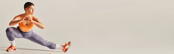 Autostima, positività corporea, donna flessibile e con i capelli corti che allunga le gambe su sfondo grigio, modello di fitness curvy in abbigliamento sportivo, atletico e sicuro di sé, potenziamento, motivazione, banner — Foto stock