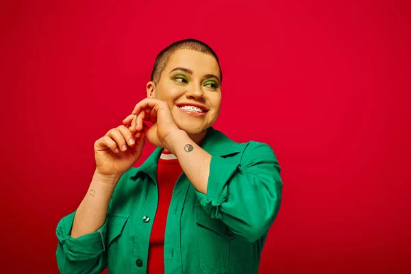 Fashion and style, cheerful and short haired woman in green outfit posing with raised hands on red background, generation z, youth culture, modern backdrop, individuality, personal style — Stock Photo