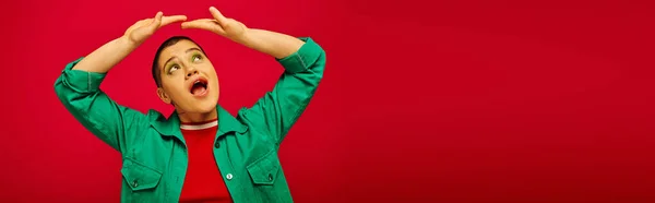 Fashion and style, amazed and short haired woman in green outfit posing with raised hands on red background, looking up generation z, youth culture, vibrant backdrop, personal style, banner — Stock Photo