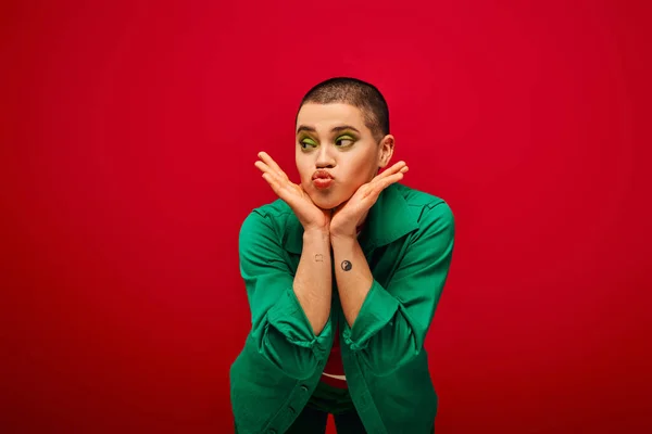 Mode und Stil, emotional und tätowiert, kurzhaarige Frau im grünen Outfit schmollende Lippen auf rotem Hintergrund, Wegschauen, Generation Z, Jugendkultur, lebendige Kulisse, Glamour — Stockfoto