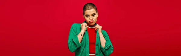 Fashion choices, emotional and tattooed, short haired woman in green outfit pouting lips on red background, looking at camera, generation z, youth culture, vibrant backdrop, style, banner — Stock Photo
