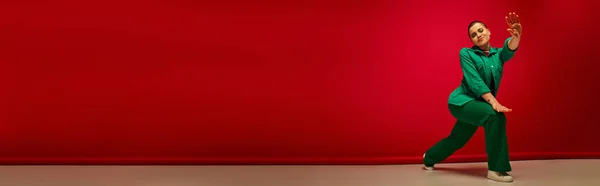 Moda y estilo, telón de fondo vibrante, mujer alegre y joven en traje elegante posando sobre fondo rojo, longitud completa, generación z, cultura juvenil, estilo personal, moda con curvas, bandera - foto de stock