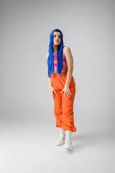 Déclaration de mode, jeune femme tatouée aux cheveux bleus posant en vêtements colorés sur fond gris, pleine longueur, individualisme, style moderne, mode urbaine, couleur vibrante, modèle — Photo de stock