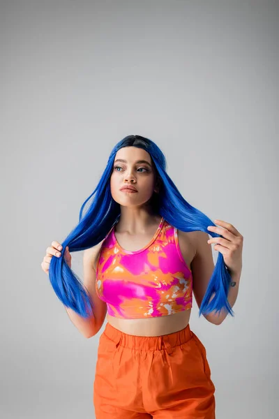Energia jovem, mulher jovem tatuada com cabelo azul posando em roupas coloridas em fundo cinza, individualismo, estilo moderno, moda urbana, cor vibrante, declaração de moda — Fotografia de Stock