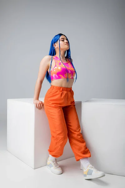 Fashion trends, tattooed young woman with blue hair posing in colorful clothes near white cubes on grey background, full length, individualism, modern style, urban fashion, vibrant color, model — Stock Photo