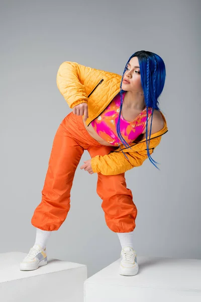 Full length, fashion and beauty trends, tattooed woman with blue hair posing in colorful clothes on grey background, standing on white cubes, individualism, urban fashion, generation z — Stock Photo
