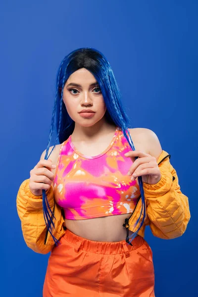 Beauty trends, dyed hair, tattooed model with blue hair posing in puffer jacket on blue background, vibrant color, urban fashion, individualism, young woman looking at camera — Stock Photo