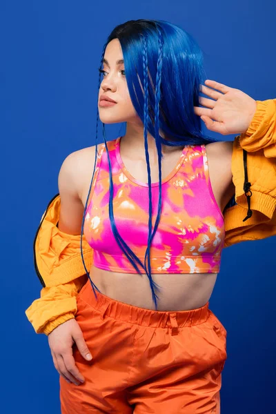Bunte Kleidung, gefärbte Haare, weibliches Model mit blauen Haaren posiert in Pufferjacke auf blauem Hintergrund, lebendige Farbe, urbane Mode, Individualismus, junge Frau mit flippigem Look — Stockfoto