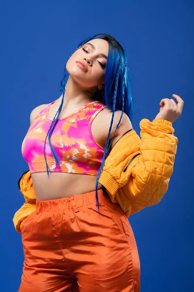 Colorful clothes, dyed hair, female model with blue hair posing in puffer jacket on blue background, hand in pocket, vibrant color, urban fashion, individualism, young woman with funky look — Stock Photo