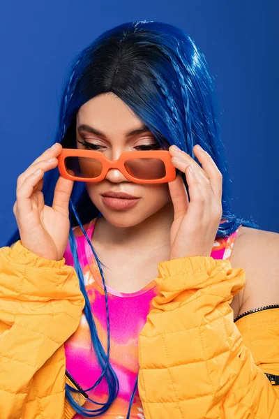 Declaración de moda, modelo femenino joven con cabello azul y trenzas que usan gafas de sol de moda aisladas sobre fondo azul, generación z, estilo rebelde, ropa colorida, individualismo, mujer moderna - foto de stock