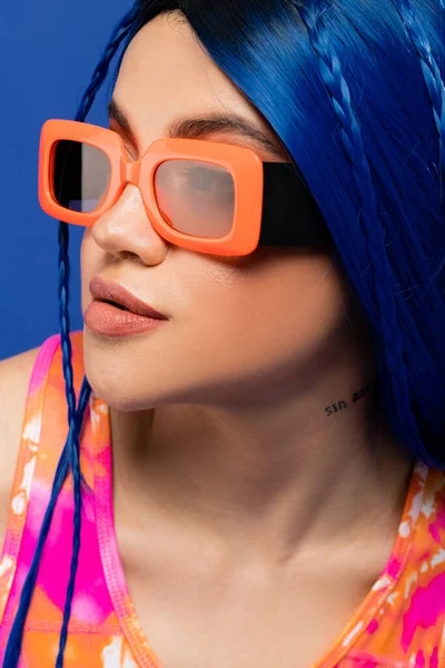 Retrato, accesorio de moda, modelo femenino joven con pelo azul y gafas de sol de moda aisladas sobre fondo azul, generación z, estilo rebelde, ropa colorida, individualismo, mujer moderna - foto de stock