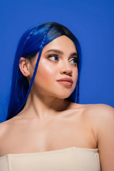 Piel brillante, mujer joven con el pelo teñido posando sobre fondo azul, color de pelo, individualismo, modelo femenino con maquillaje y peinado de moda, juventud vibrante, perfección de la piel - foto de stock