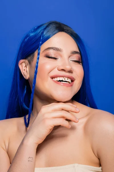 Beauty concept, happy young woman with dyed hair posing on blue background, hair color, individualism, female model with makeup and trendy hairstyle smiling with closed eyes, vibrant youth — Stock Photo