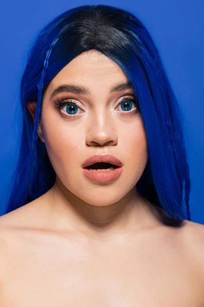 Konzept der Schönheitstrends, Porträt einer schockierten jungen Frau mit gefärbten Haaren, die auf blauem Hintergrund posiert, Haarfarbe, Individualismus, weibliches Model mit Make-up und trendiger Frisur, lebendige Jugend, emotionale — Stockfoto