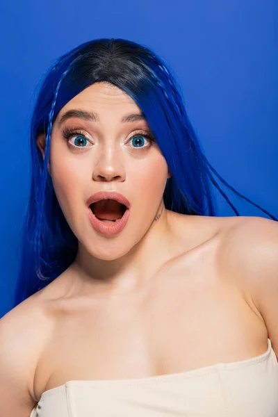 Shocked, portrait of emotional young woman with dyed hair posing on blue background, hair color, individualism, female model with makeup and trendy hairstyle, vibrant youth — Stock Photo