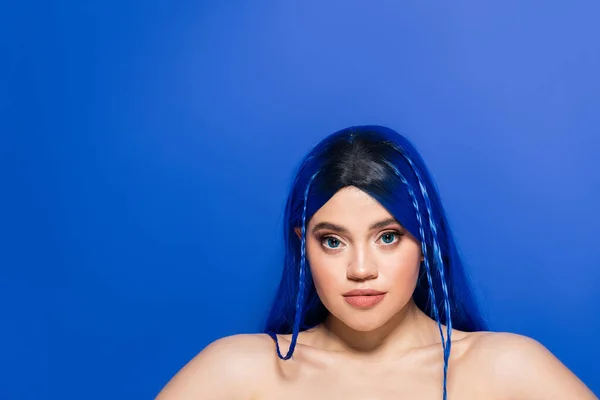 Individualismus, Porträt einer jungen Frau mit gefärbten Haaren und glühender Haut, die auf blauem Hintergrund posiert, Haarfarbe, Individualismus, weibliches Model mit Make-up und trendiger Frisur, lebendige Jugend — Stockfoto