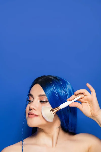 Schönheitstrends, Individualismus, junge Frau mit lebendigem Haar mit Kosmetikpinsel auf blauem Hintergrund, Kosmetik, Selbstdarstellung, Make-up, Visage, Jugendkultur, weibliches Modell — Stockfoto