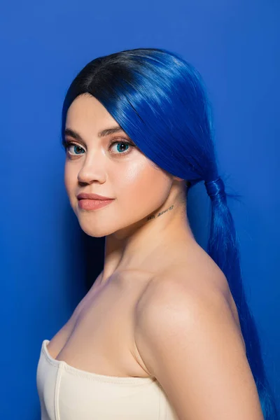 Glowing skin concept, portrait of tattooed young woman with vibrant hair color posing with bare shoulders on bright blue background, youth, individualism, beauty trends, unique identity — Stock Photo