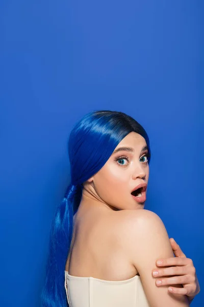 Modelo emocional, retrato de mujer joven conmocionada con color de pelo vibrante posando con hombros desnudos sobre fondo azul, juventud, tendencias de belleza, identidad única, bandera - foto de stock