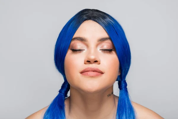 Sous-culture moderne, femme tatouée avec les yeux fermés et les cheveux bleus posant sur fond gris, coiffure, couleur vibrante, beauté moderne, expression de soi, individualisme — Photo de stock