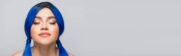 Subcultura moderna, mujer tatuada con los ojos cerrados y el pelo azul posando sobre fondo gris, peinado, color vibrante, belleza moderna, expresión personal, individualismo, bandera - foto de stock