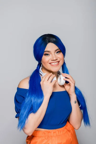 Musikliebhaberin, fröhliche junge Frau mit blauen Haaren und kabellosen Kopfhörern, die auf grauem Hintergrund lächelt, lebendige Jugend, Individualismus, moderne Subkultur, Selbstausdruck, Tätowierung, Sound — Stockfoto