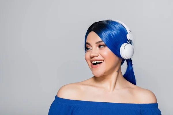 Self expression, music lover, happy young woman with blue hair listening music in wireless headphones on grey background, vibrant youth, individualism, modern subculture, tattoo, sound — Stock Photo