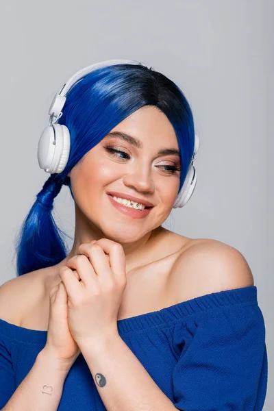 Selbstausdruck, fröhliche junge Frau mit blauen Haaren, die Musik in drahtlosen Kopfhörern auf grauem Hintergrund hört, lebendige Jugend, Individualismus, moderne Subkultur, Tätowierung, Sound — Stockfoto
