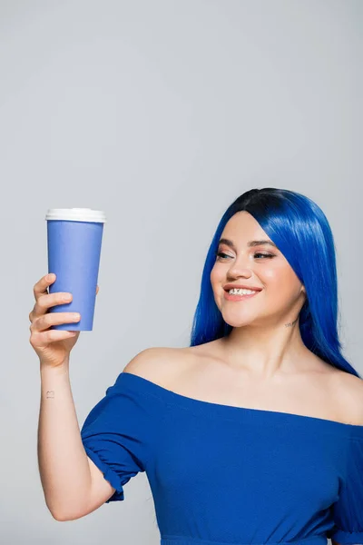 Бумажная чашка, энергия, счастливая молодая женщина с голубыми волосами и глазами держа кофе идти на сером фоне, вынос, кофеин, татуировка, яркий цвет, самовыражение, индивидуализм — стоковое фото