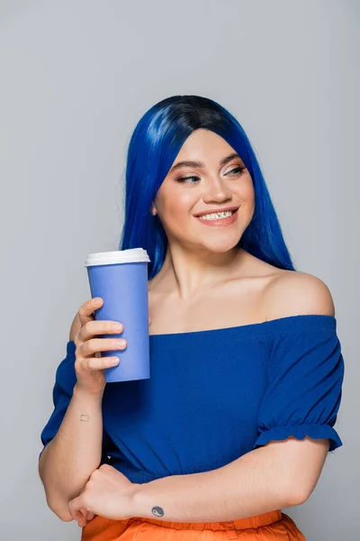 Positivity, disposable cup, young woman with blue hair and eyes holding coffee to go on grey background, takeaway, caffeine, energy, tattoo, vibrant color, self expression, individualism — Stock Photo