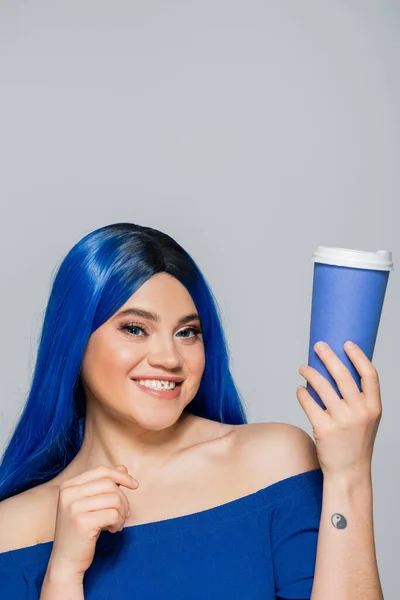 Паперова чашка, щаслива молода жінка з блакитним волоссям і очима тримає каву на сірому фоні, витягування, кофеїн, енергія, татуювання, яскравий колір, самовираження, індивідуалізм — стокове фото