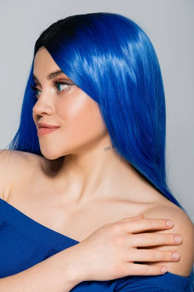 Piel brillante y juventud, mujer tatuada con el pelo teñido azul mirando hacia otro lado sobre fondo gris, peinado, cabello azul, belleza moderna, expresión personal, individualismo, modelo femenino - foto de stock
