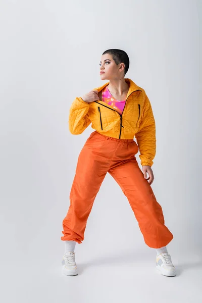 Outerwear, casual attire, tattooed and young woman with short hair pulling yellow puffer jacket on grey background, urban fashion, vibrant youth, trendy outfit, stylish look, studio photography — Stock Photo