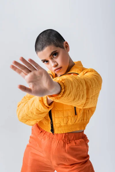 Outerwear, casual attire, fashion model posing with outstretched hand, young woman with short hair wearing yellow puffer jacket on grey background, isolated, studio photography, youth culture — Stock Photo