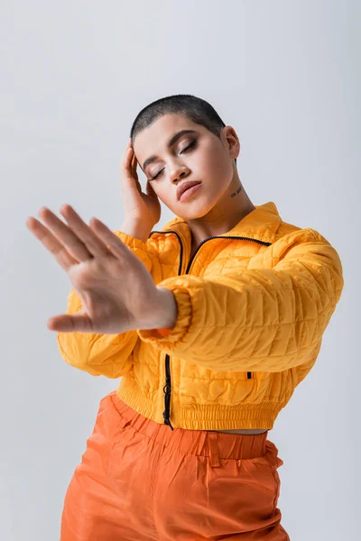Outerwear, casual attire, fashion model posing with outstretched hand, young woman with short hair and closed eyes in yellow puffer jacket on grey background, isolated, youth culture — Stock Photo