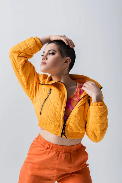 Верхняя одежда, мода заявление, модель смотрит в сторону, молодая женщина с короткими волосами позирует в желтой куртке фугу на сером фоне, изолированные, молодежная культура, повседневная одежда, стильный вид — стоковое фото